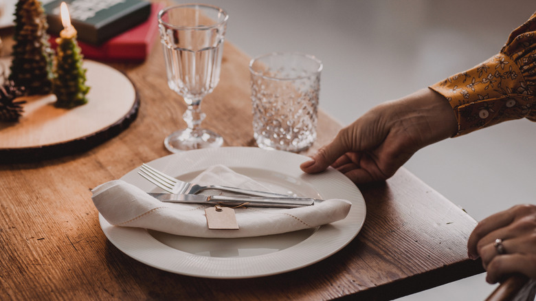 Hands placing white plate and cutlery on wood table