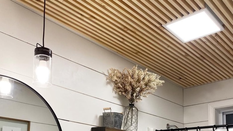 A bathroom ceiling with wood slates and square light.