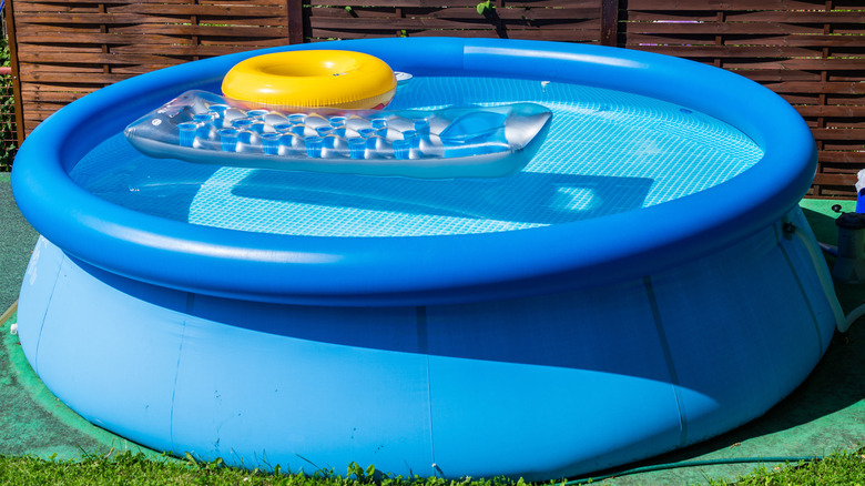 An inflatable pool on a green mat with an inner tube and an inflatable lounger inside