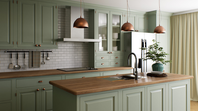 A kitchen with muted green cabinets and wood countertops