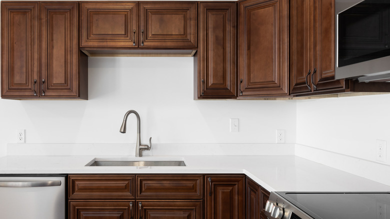 A kitchen with dark wood cabinets and white countertops.