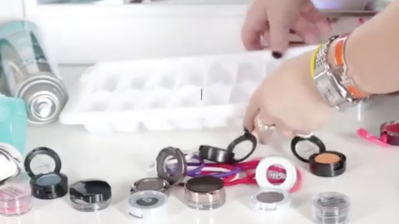 a woman putting an ice cube tray down behind eyeshadows