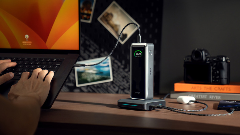 Hands typing on laptop charged by Anker device
