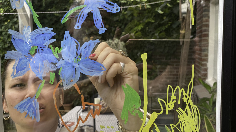Woman painting blue flowers onto window