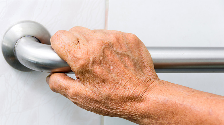 An elderly person's hand holds a steel grab bar