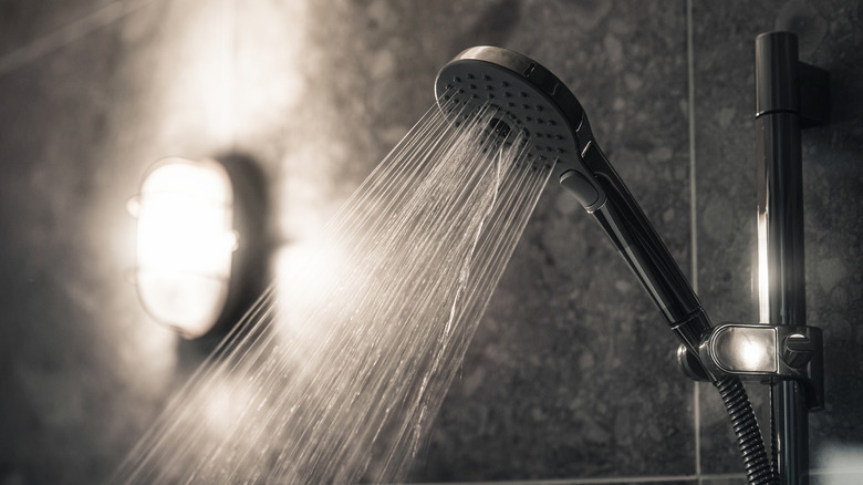 Close-up of a black showerhead with water coming out of it in a black tiled bathroom