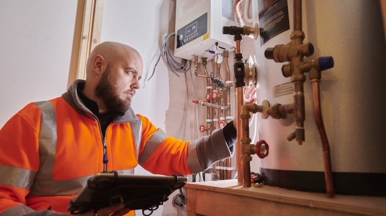 A man in an orange safety jacket inspects copper pipes in a boiler room