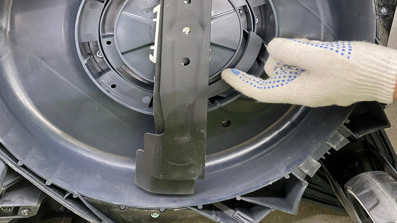 A gloved hand replacing the blades of a lawn mower.