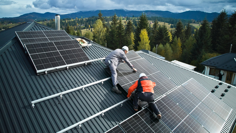 Electricians installing solar panels on roof of house