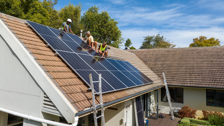 Workers on roof install photovoltaic (PV) solar panels