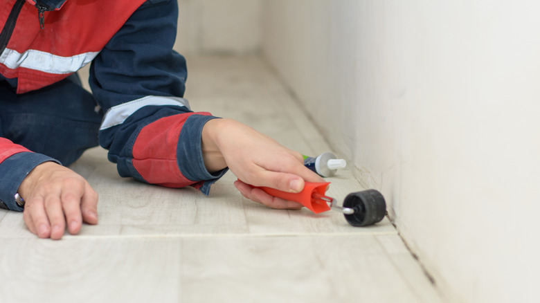 A person uses a handheld roller to adhere a sheet of linoleum flooring