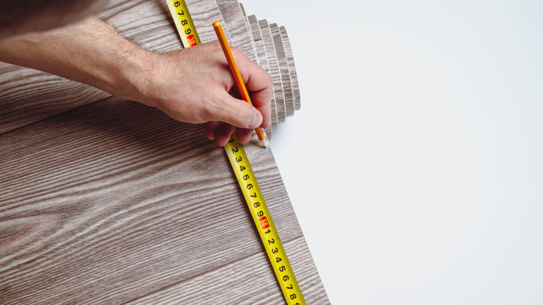 A man uses a yellow measuring tape to mark a roll of linoleum