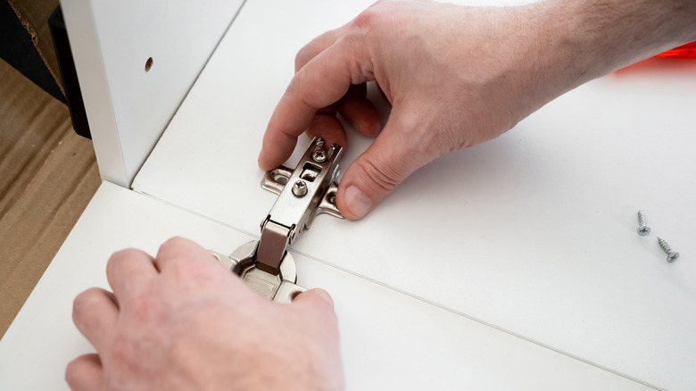 Person fitting a hinge onto the bottom of a cabinet