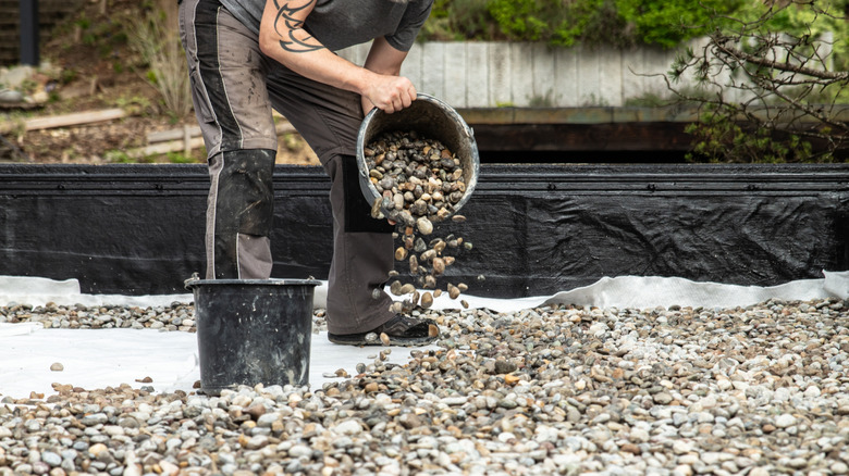 Man pouring gravel onto the ground on top of a ground cover