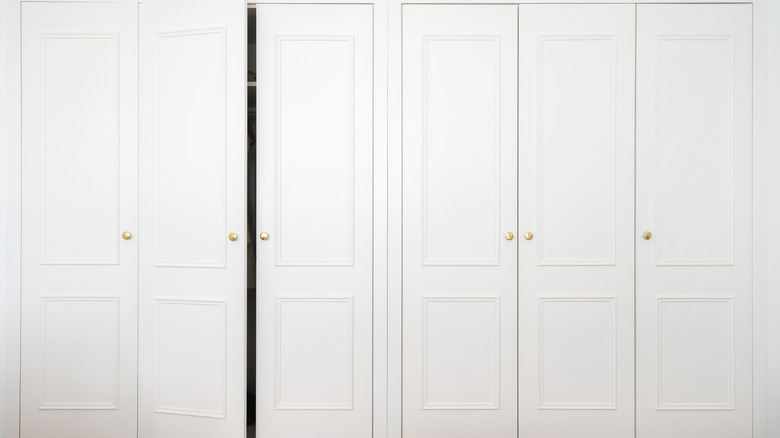 three sets of white closet doors with one door slightly ajar