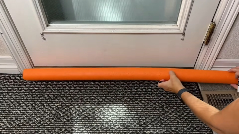 a woman uses a pool noodle to create an easy diy draft stopper
