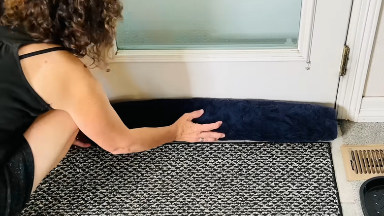 a woman uses a rolled up towel to block a draft under her door