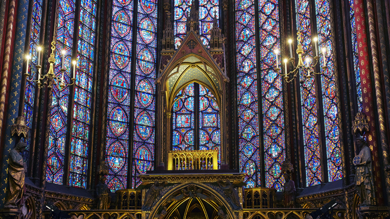 A cathedral is lined with innumerable pieces of stained glass that form a surrounding wall of murals