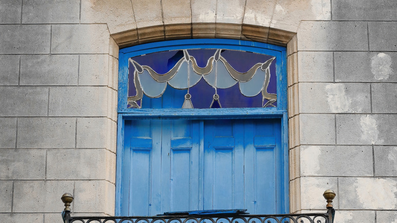 A stained glass transom is featured at the top of a blue door, set in a wooden frame.