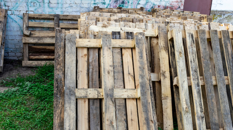 A cluster of wood pallets lean against a brick wall.