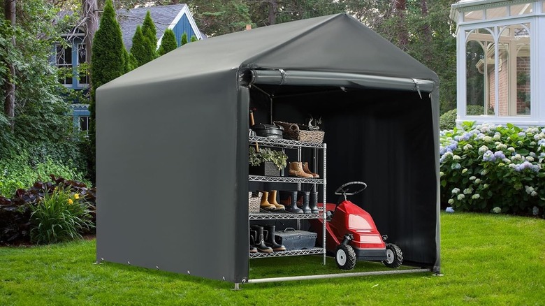 A black Mellcom 5 x 7 foot canopy shed in a backyard with a lawn mower and storage shelf inside and the door rolled up