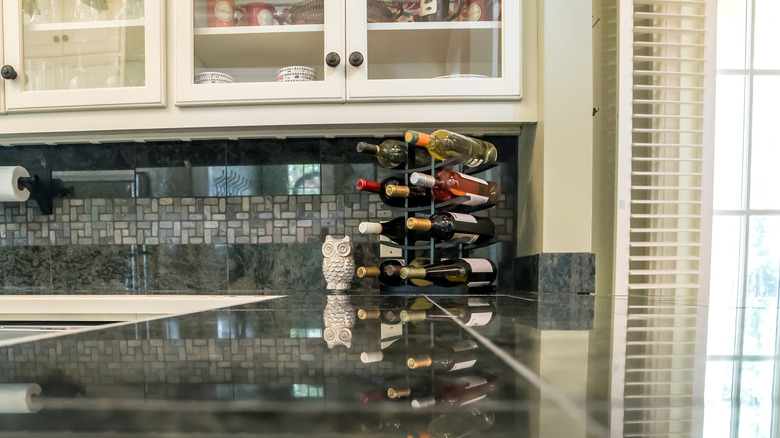 A modern kitchen with a shiny black countertop and white cabinets with an owl statue and a wine rack.