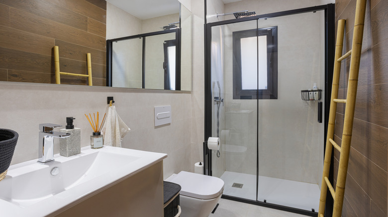 A bathroom features a walk-in shower framed by black metal, with a bamboo ladder sitting in front.