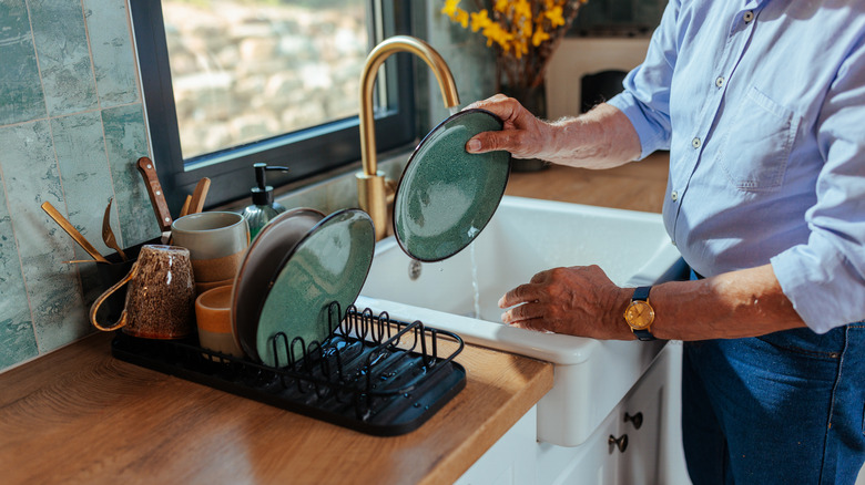 Closeup of man placing clean dishes on a drying rack next to the sink