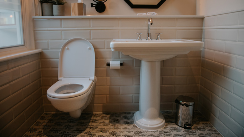 A bathroom interior with a toilet, sink, and mirror against tiled walls