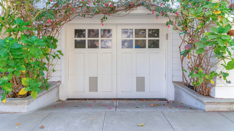 White house with hinged garage doors  and creeping plants