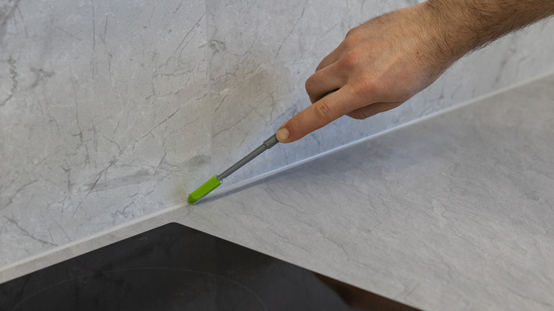 A person tools a bead of white silicone sealant to smooth it out