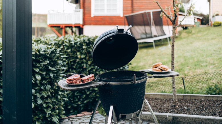 A BBQ in a backyard with burgers on one side and buns on the other
