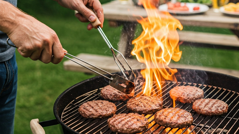 A person grilling burgers over the open flame of a barbecue