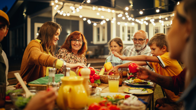 A happy family gathered outside around a patio table sharing food and drinks.