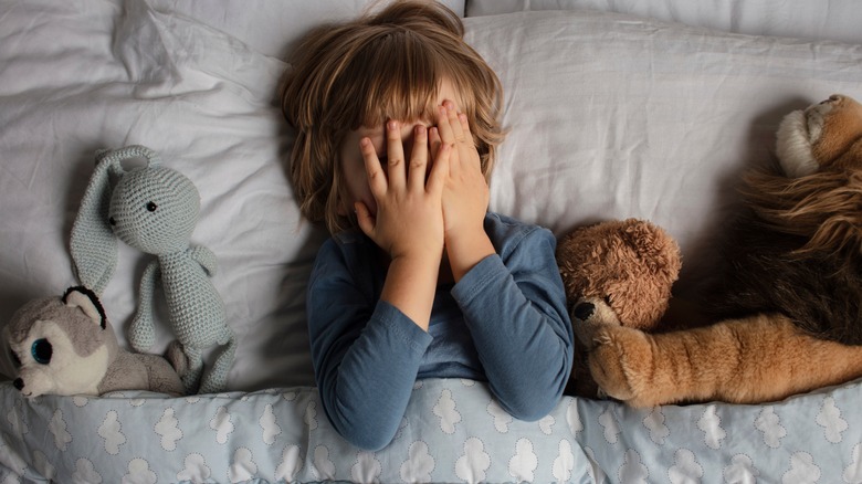 child covering face in bed