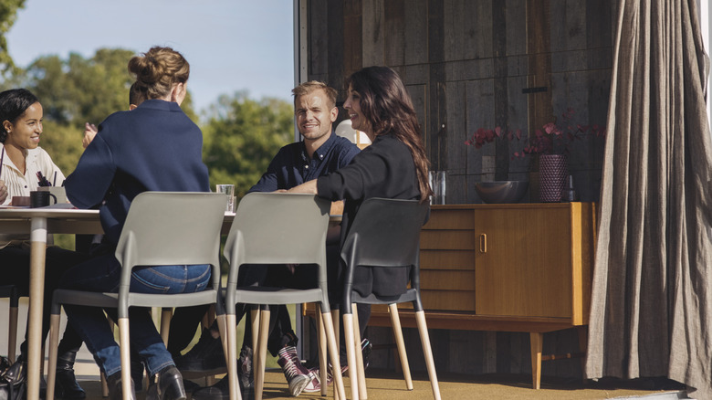Group of friends gathering outdoors at a table, seated next to a buffet cabinet.
