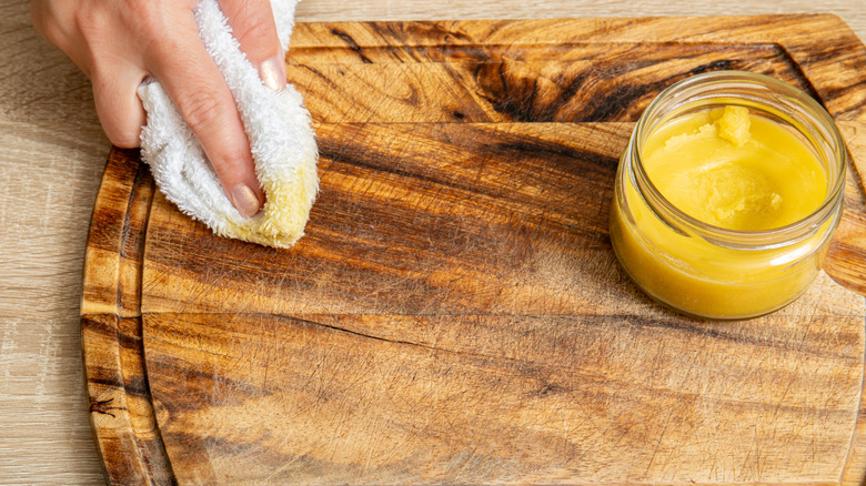 A hand conditioning a cutting board with beef tallow.
