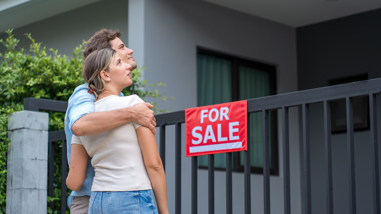 A young couple looking at a home with a for sale sign in front.