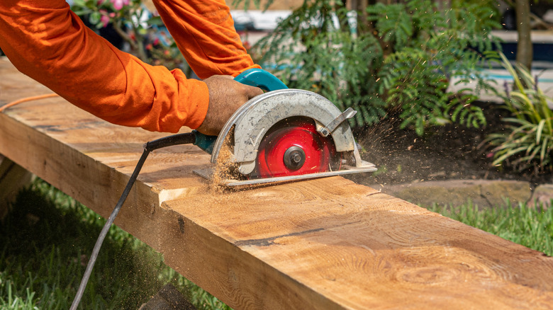 man cutting large piece of wood with hand saw outside
