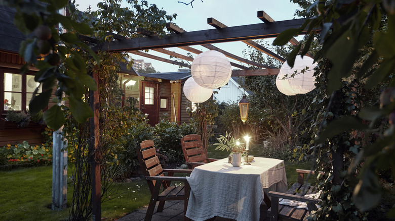 pergola with dining table underneath in backyard with creeping vines and paper lanterns