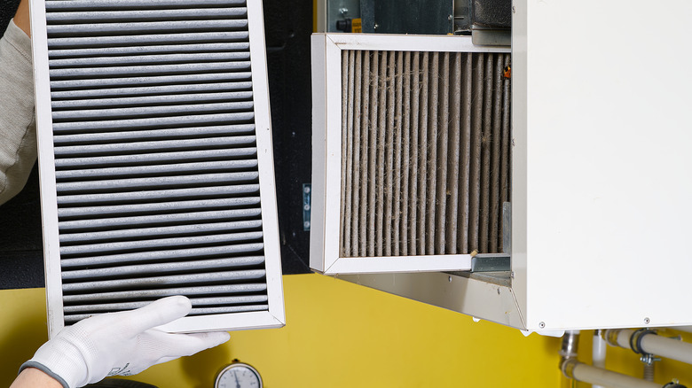 A person holds a new air filter next to a dirty filter in an HVAC handler