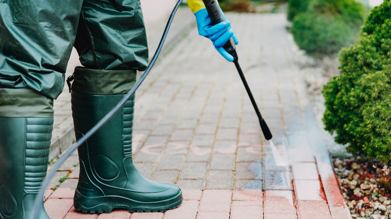 A person using a pressure washer to clean pavers
