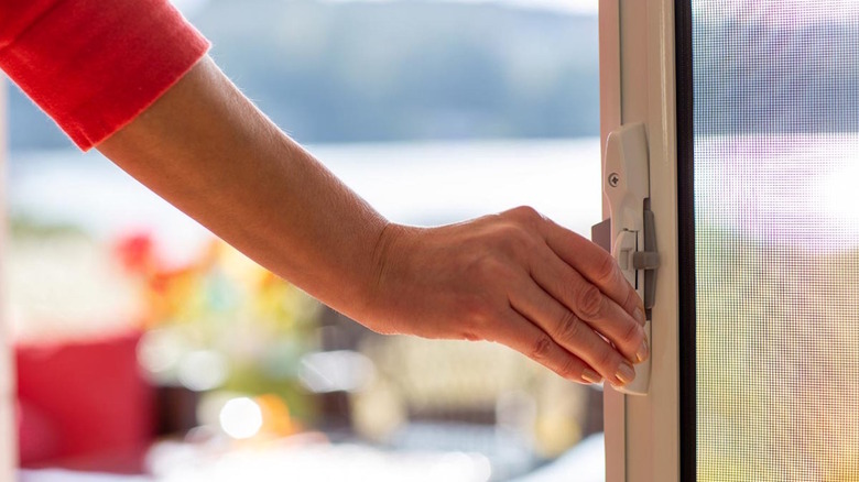 A woman's hand rests on the handle for a screen door.
