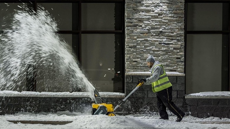 Man using a DeWalt snow blower near a building