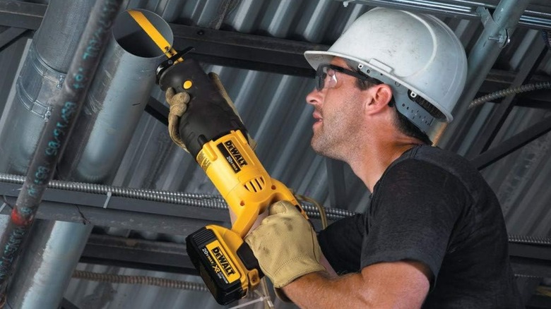 A person cutting metal pipe installed below ceiling in a building