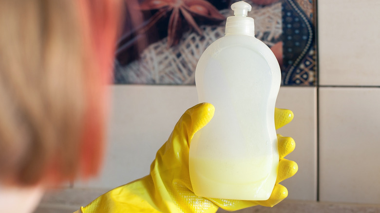 Hand with yellow glove holding a bottle of dish soap