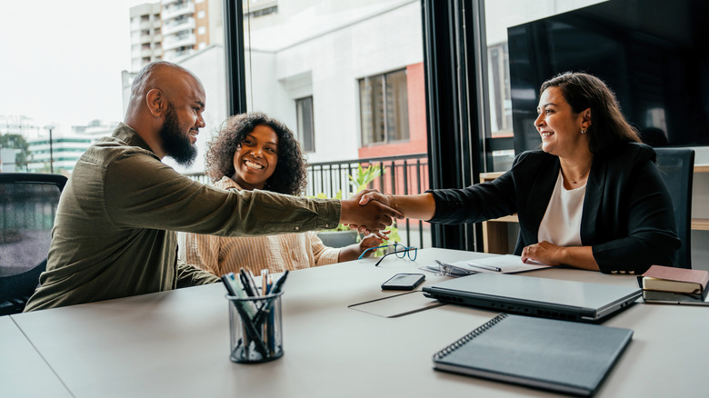 A couple shakes hands with a real estate agent in an office