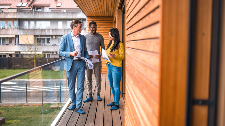 A real estate agent and a middle-aged couple stand on the balcony of a condo