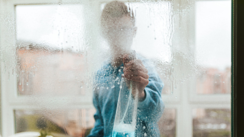 Person spraying window cleaner on the surface, the glass covered in droplets