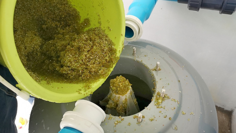 A bucket of glass media being added to a pool filter.